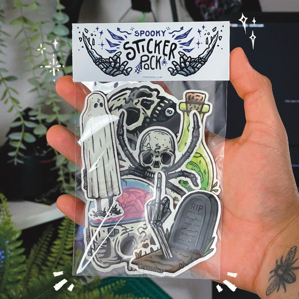 植物を背景に、手に持ったステッカーパック。「SPOOKY STICKER PACK」と書かれたヘッダーが付いていて、不気味なテーマのイラストステッカーが入っています。