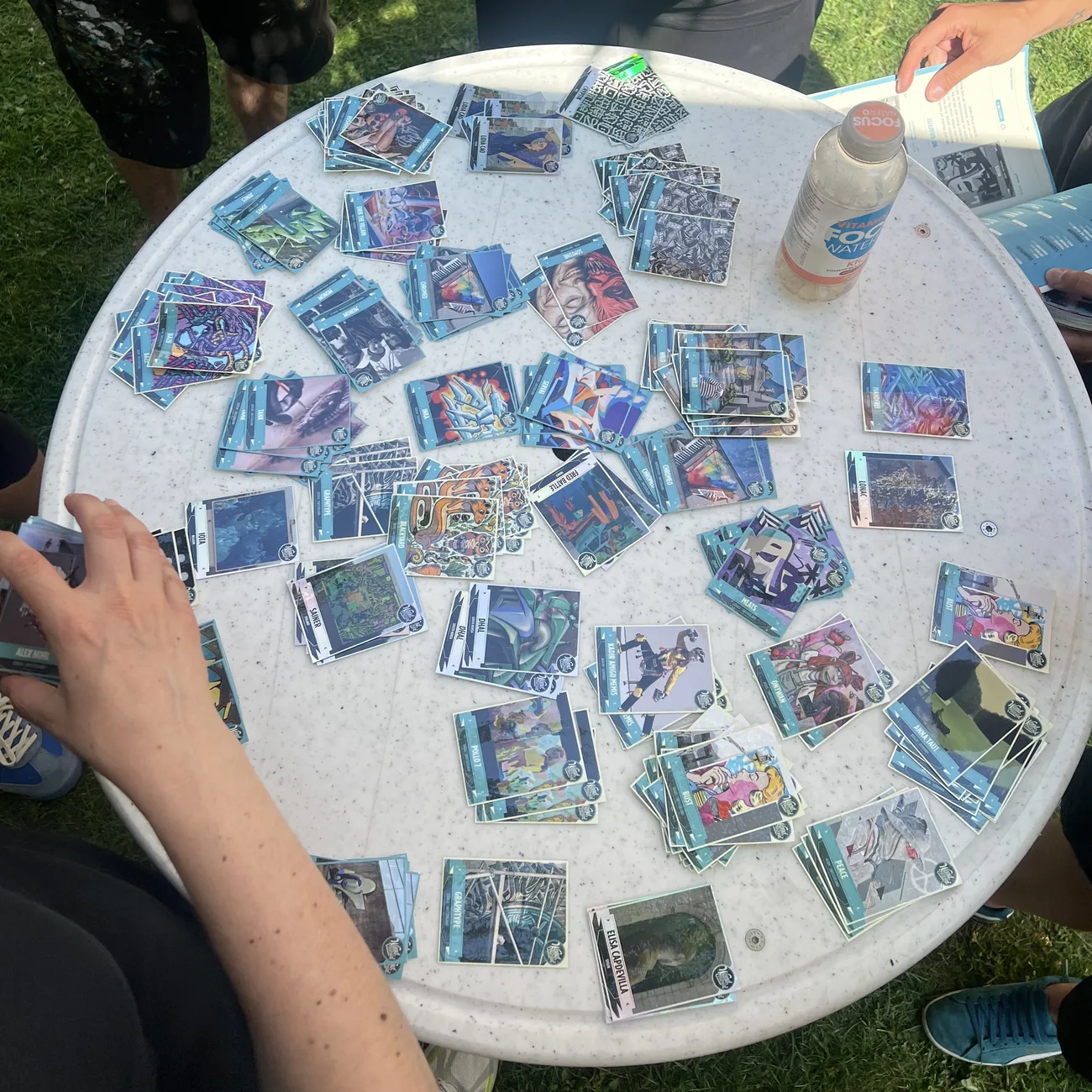 丸テーブルに広げたストリートアートのコレクションステッカーで青いステッカーアルバムを埋めるフェスティバルの来場者