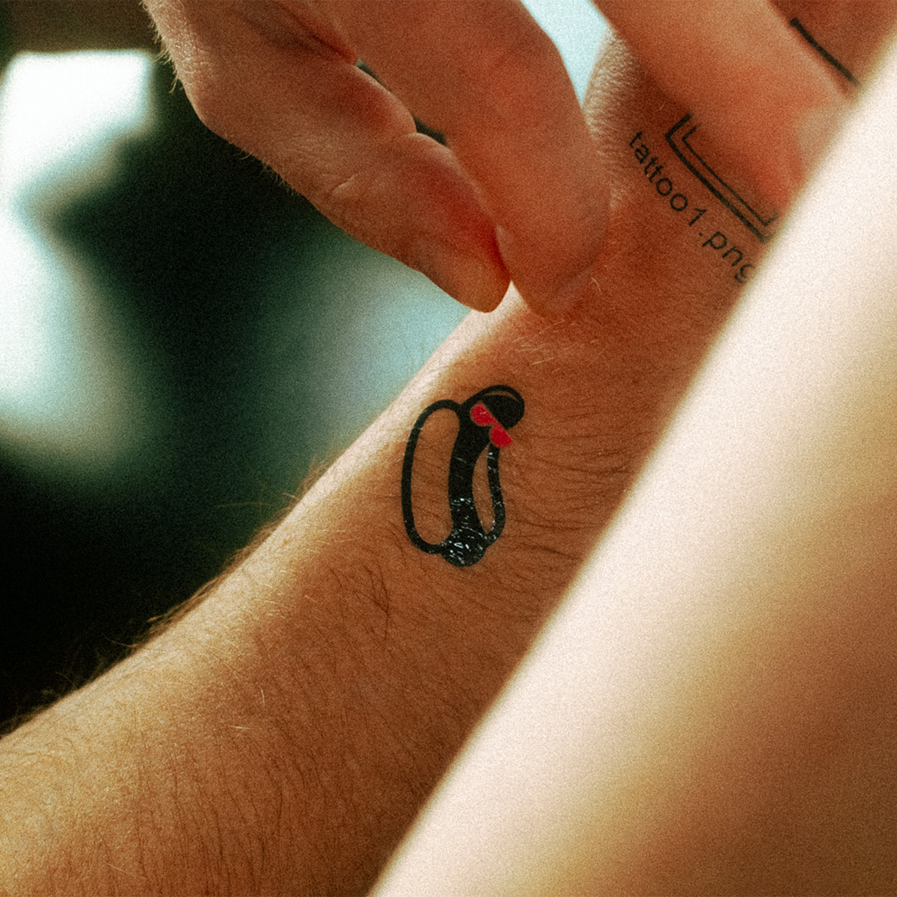 Close-up of a wrist with a small hot dog temporary tattoo, as another hand gently touches the skin.