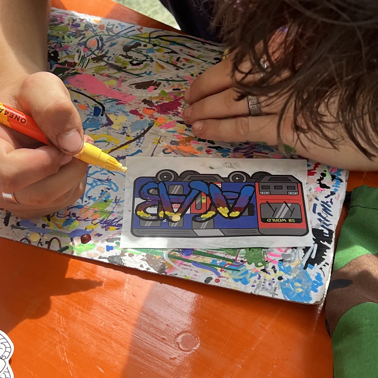 Brainfart x StickerAppのワークショップで、S8 Worldの電車ラベルを黄色のペイントマーカーで塗る手元