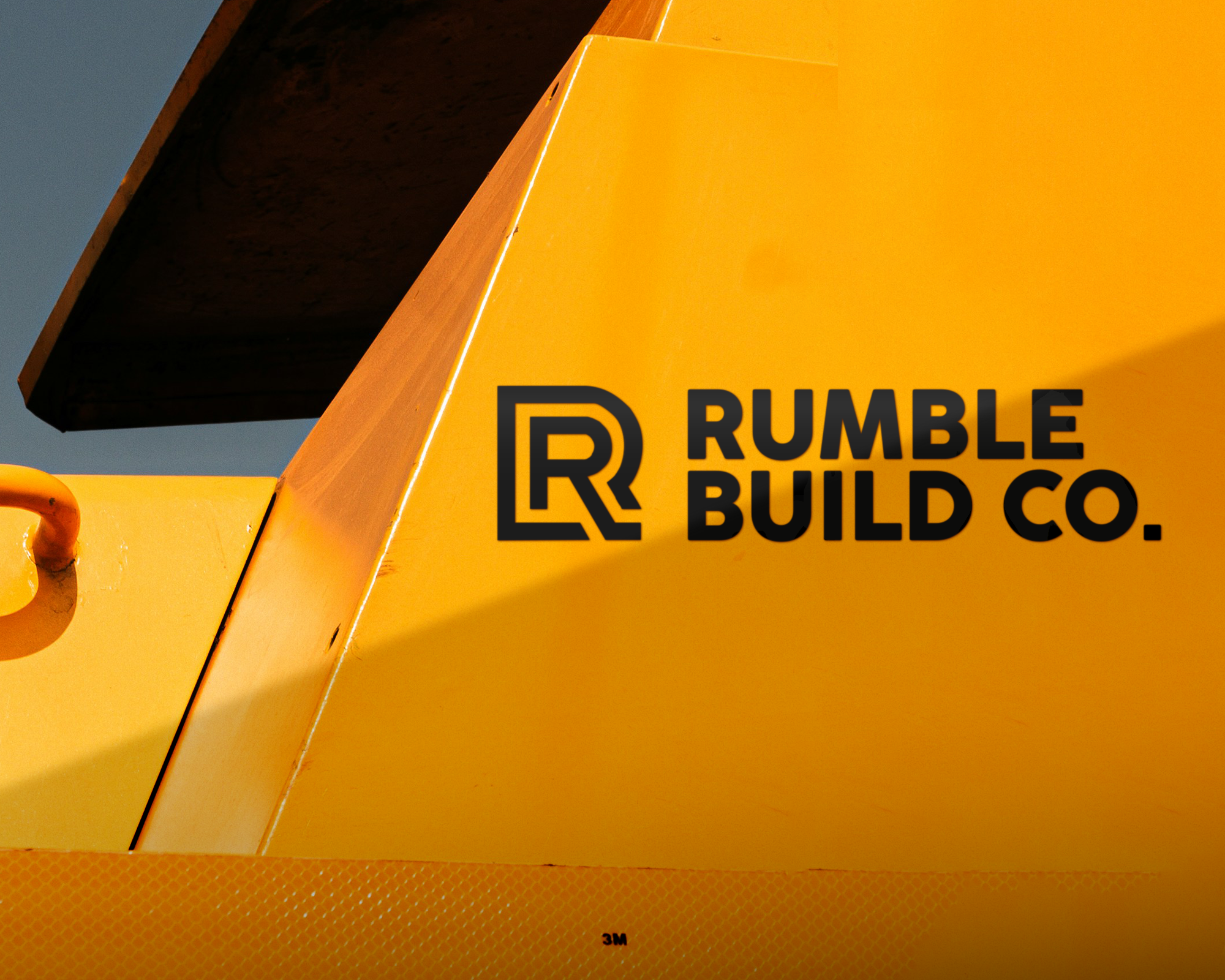 黄色の産業用車両のクローズアップ。表面に「Rumble Build Co.」のVinyl Transferが太字で描かれ、抽象的な「R」デザインが特徴です。
