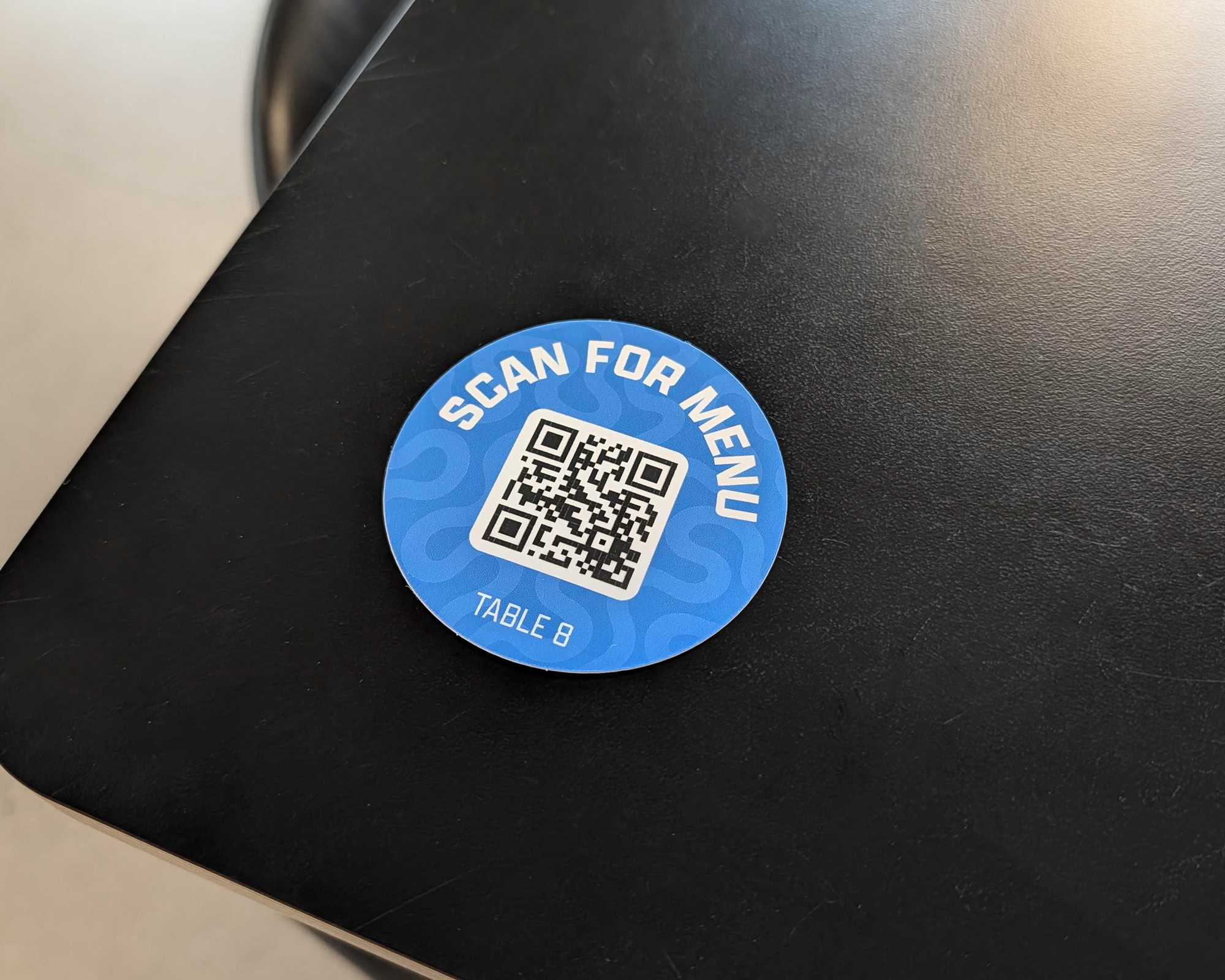 黒いテーブルに貼られた、テーブル8用の「Scan for menu」青色QRコードステッカー