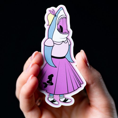 Vinyl sticker of an open mouthed shark in a pink skirt held by a hand