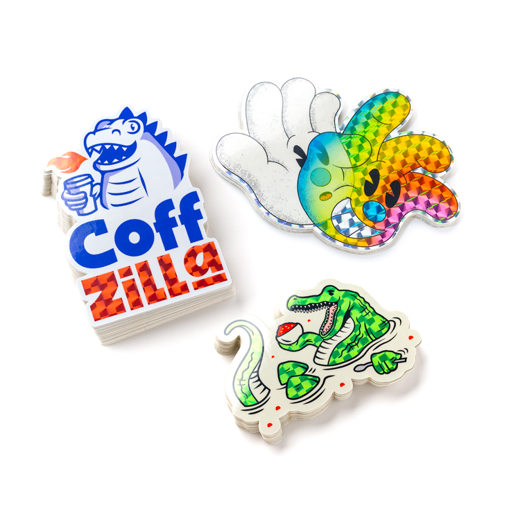 Three die-cut stickers featuring a hand, Godzilla, and a crocodile with prismatic effect, on a white background.